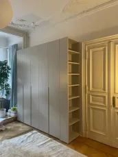 Custom wardrobe with side library: the modern, design wardrobe perfectly matches the old-style apartment in the center of Berlin in Germany - RAL7047 matt lacquered with integrated handles.

The side library, matching the wardrobe in color, adds a stylish and cohesive look to the space. It’s ideal for displaying plants, handbags, books, or decorative items like photo frames, art pieces, or even small storage baskets, seamlessly combining the functionality of the room with elegant design.

The exact measurements of this wardrobe are 231.2 cm in width, 275 cm in height, and 61 cm in depth.