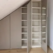 Accesorios interiores del armario mostrado en esta imagen:

- estantes de 35 mm de grosor hechos de melamina efecto madera, color marfil.

Armario bajo techo inclinado: cada techo tiene una pendiente diferente, por lo que ofrecemos nuestro configurador, que se adapta perfectamente a sus medidas para crear un diseño de armario práctico y funcional, personalizado según sus necesidades. Todo está cuidadosamente oculto detrás de puertas de color personalizado. Este armario está instalado en la casa de nuestro cliente en Watt, Suiza - FB 243 Charleston Gray lacado mate con asas integradas.