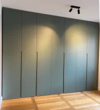 Armadio su misura: Installato nella camera da letto del nostro cliente a Berlino, Germania, questo colore verde varia a seconda della luce (luce naturale o illuminazione artificiale).

Con un&rsquo;illuminazione calda nella stanza e i riflessi del pavimento in legno, assume una tonalità di verde morbida e calda (come mostrato nell&rsquo;immagine), creando un’atmosfera accogliente e naturalmente rilassante.

Questo armadio è rifinito in laccato opaco FB 47 green smoke con maniglie integrate.

Le dimensioni esatte di questo armadio sono: 350,7 cm di larghezza, 266 cm di altezza e 61 cm di profondità.