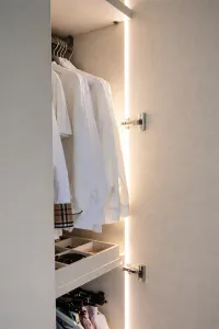 Innenausstattung des Schranks, der auf diesem Bild zu sehen ist:

- 35 mm dicke Regalböden aus Melamin mit einem Holzdekor in Elfenbeinfarbe,
- Krawatten- und Gürtel-Schublade in Elfenbeinfarbe (nur geeignet für Module mit einer Breite von 89 cm),
- LED-Leuchten integriert im Schrank (vertikale Ausrichtung),
- Kleiderstange verchromt.

Schrank nach Maß mit Seitenbücherschrank: Personalisierte Maße und eine helle Farbe, die eine frische Atmosphäre im begehbaren Raum unseres Kunden schafft – Frankfurt, Deutschland – matt lackiert in RAL1013 mit integrierten Griffen.